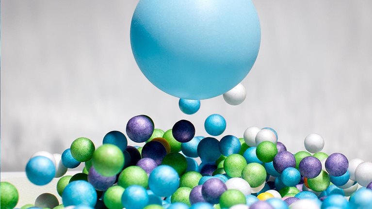 One large blue ball in mid air above many smaller blue, green, purple and white balls