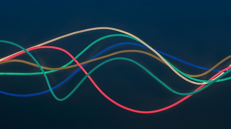 Blue, green, red, brown and white wire in wave pattern on dark blue background - stock photo