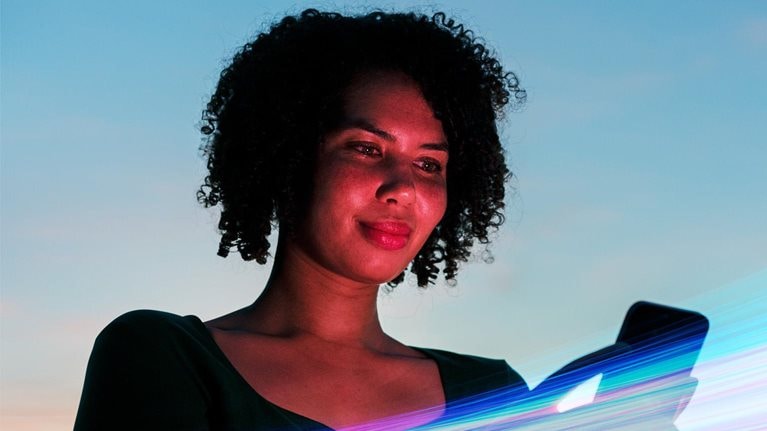 Woman using a smartphone against a vibrant blue sky backdrop, surrounded by vivid streaks of colorful light.