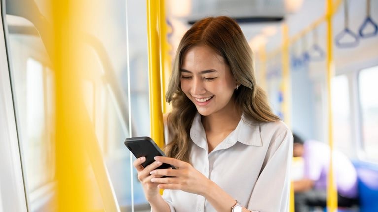 Happy young woman traveling by bus and using a smartphone. - stock photo