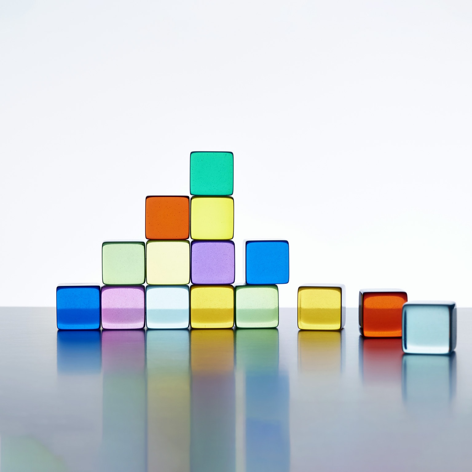 A pyramid made of vibrant transparent cubes against a white background. The pyramid is incomplete on the right side, and there are extra cubes lying next to it.