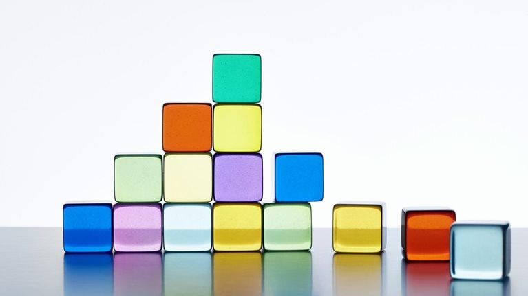 A pyramid made of vibrant transparent cubes against a white background. The pyramid is incomplete on the right side, and there are extra cubes lying next to it.