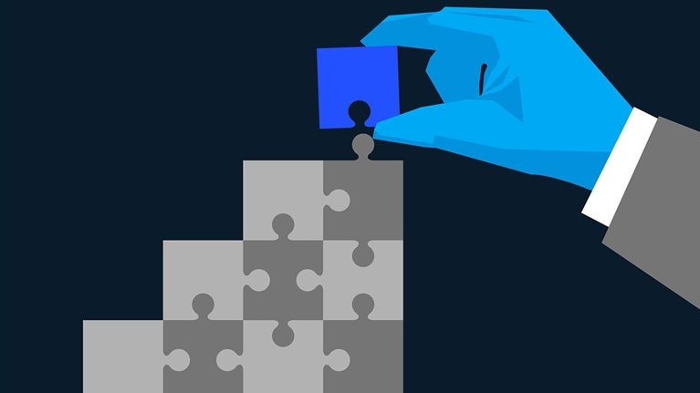 A hand is placing the final blue puzzle piece into a larger structure made of grey pieces. The image is an illustration symbolizing problem-solving, integration, or building a solution.