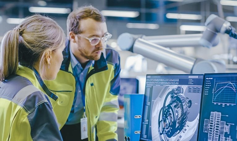 At the Factory: Male Mechanical Engineer Holds Component while Female Chief Engineer Work on Personal Computer, They Discuss Details of the 3D Engine Model Design.