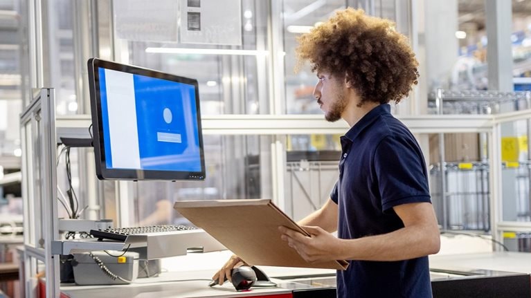 Male worker scanning a delivery package and working on computer at automated warehouse. - stock photo