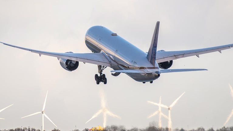plane taking off with wind turbines in background stock photo