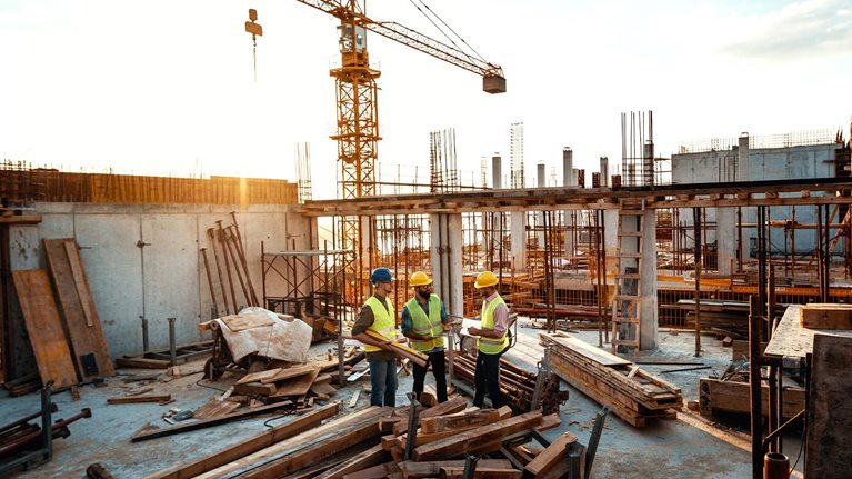Architects and engineers discussing work progress between concrete walls, scaffolds and cranes. - stock photo