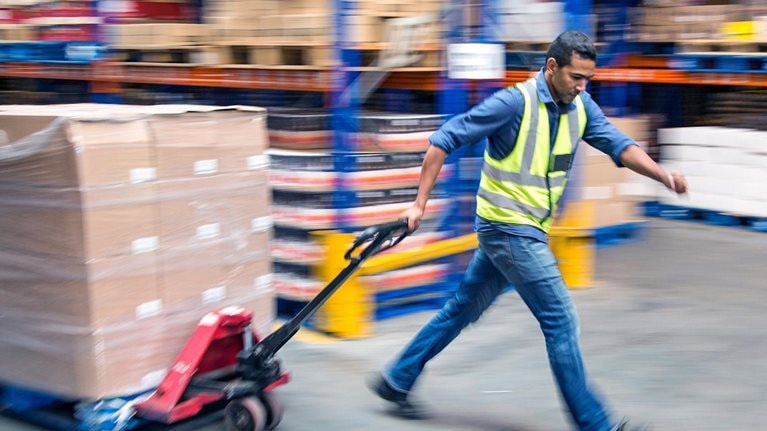 Worker pulling pallet truck inside a food distribution warehouse