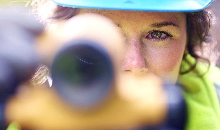 Close up of young female surveyor looking through the lens of a theodolite checking levels on a site.