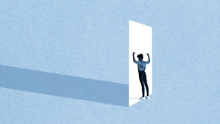 Full length of young woman flexing muscles while standing in front of white doorway against blue background