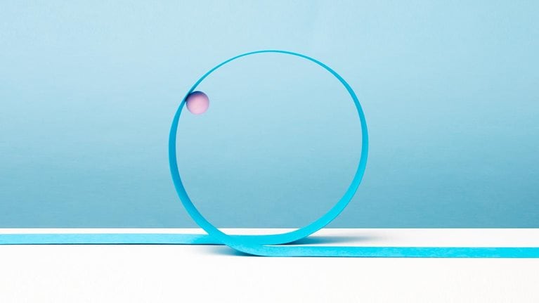 Pink ball going around blue paper loop, white surface, blue background - stock photo