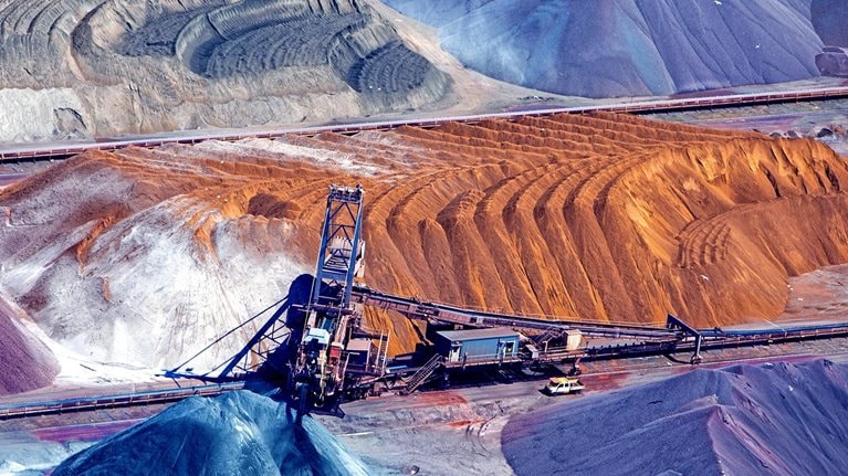 An aerial image of a piles of ore organized around a conveyor belt.