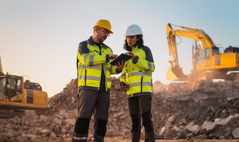 Using Tablet On Construction Site of New Apartment Complex. Real Estate Developers Discussing Business, Excavators Working.