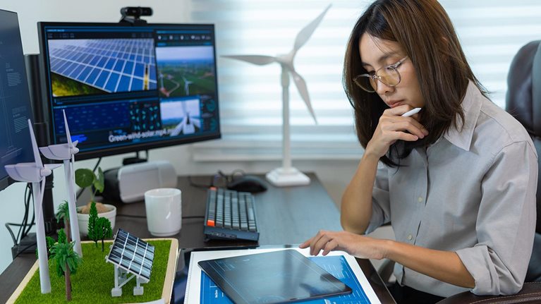 Portrait of Asian female engineer working with computer, wind turbine solar panel model for development of sustainable energy project. - stock photo