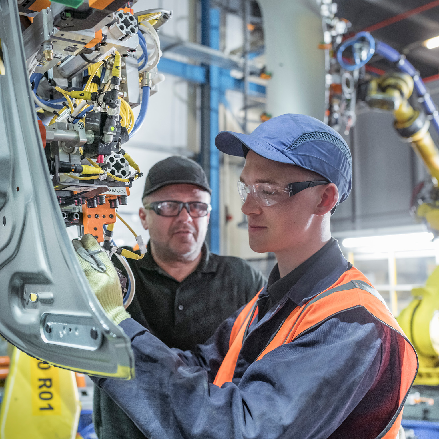Apprentice engineer with mentor and robots in car factory - stock photo