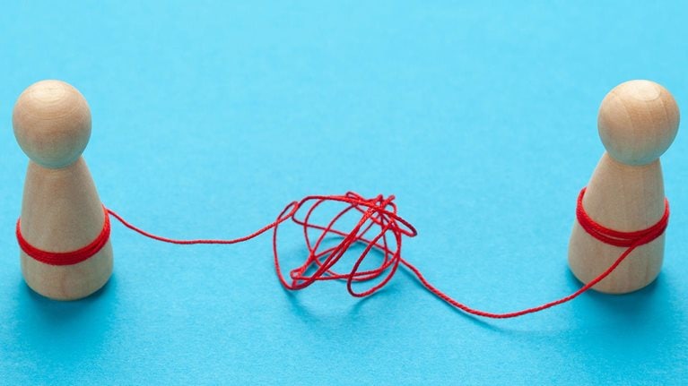 Confused relationships of people in a couple. Two wooden block figures tied together by string tangled in knots.