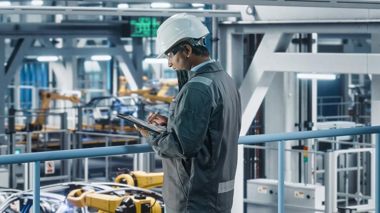 Car Factory Engineer in Work Uniform Using Tablet Computer. Automotive Industrial Manufacturing Facility Working on Vehicle Production with Robotic Arms. Automated Assembly Plant.