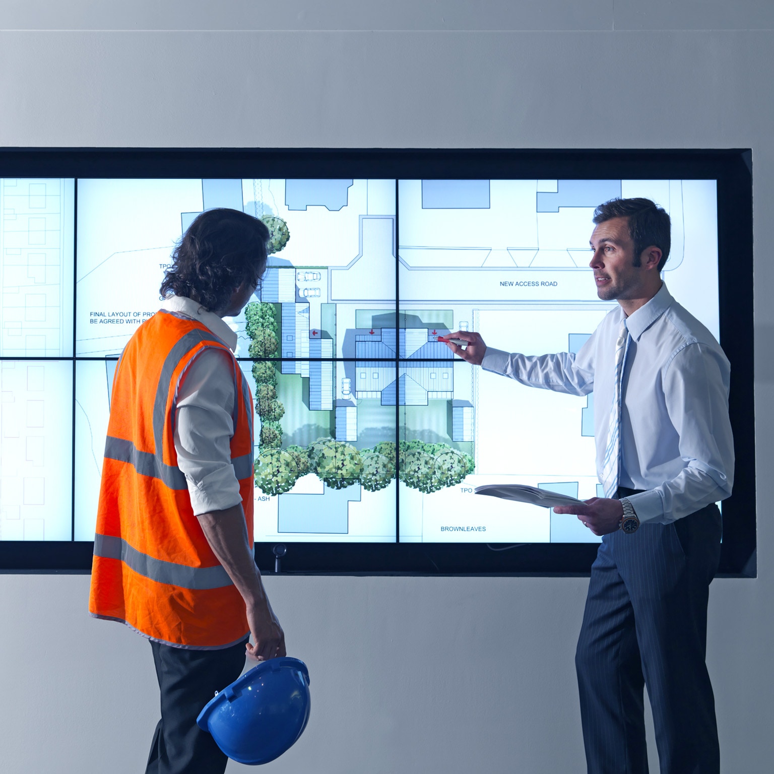 Construction worker and architect look at construction plans on digital screen