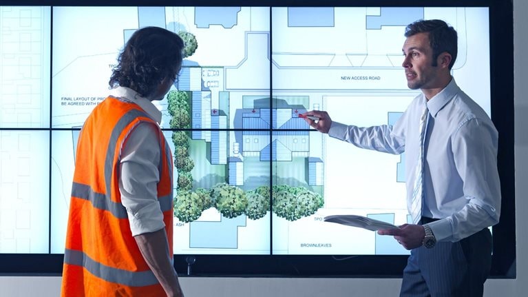 Construction worker and architect look at construction plans on digital screen