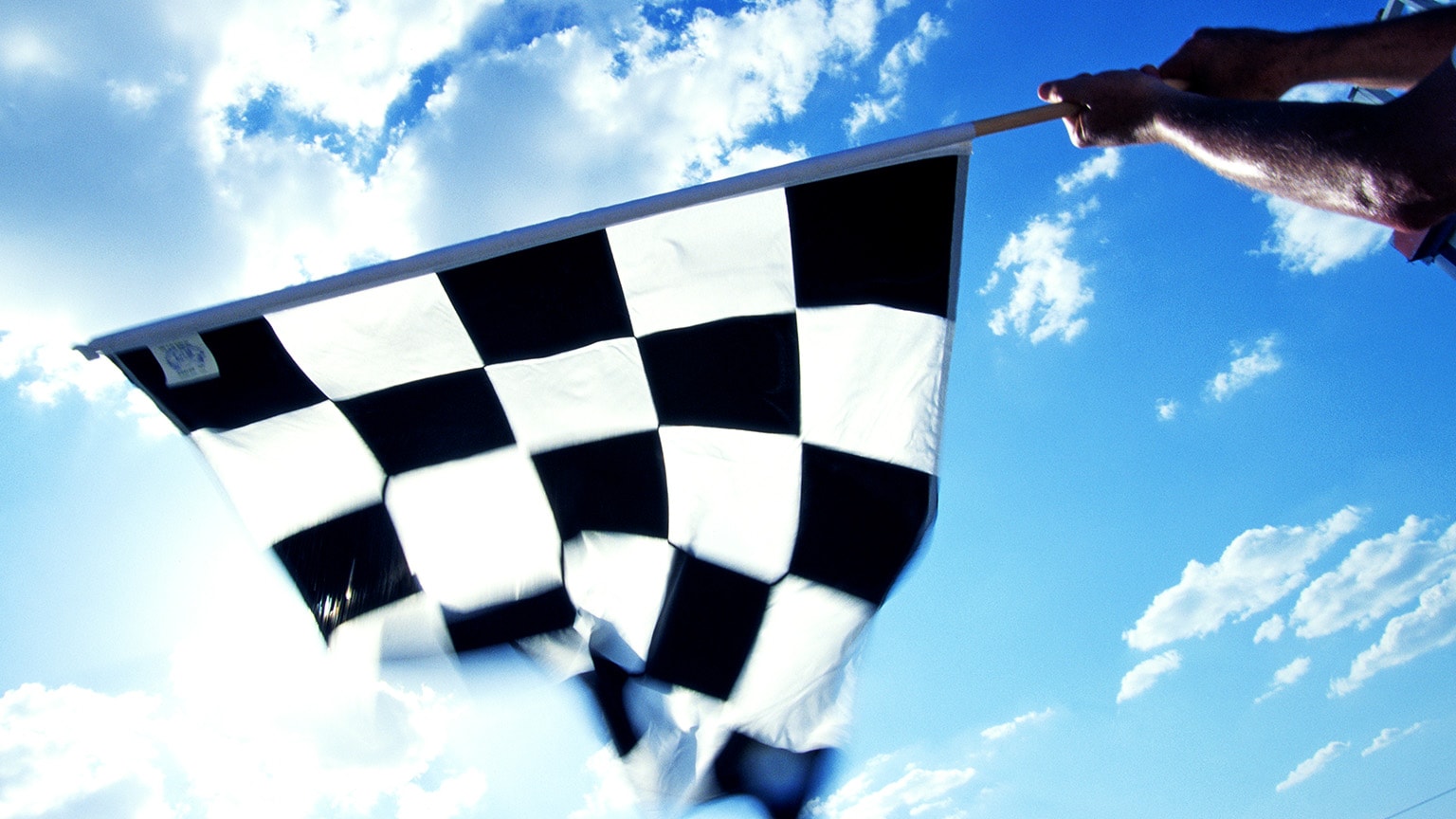 Image of a person waiving a checkered flag from the finish line.