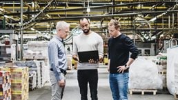 Three senior engineers using computer in warehouse