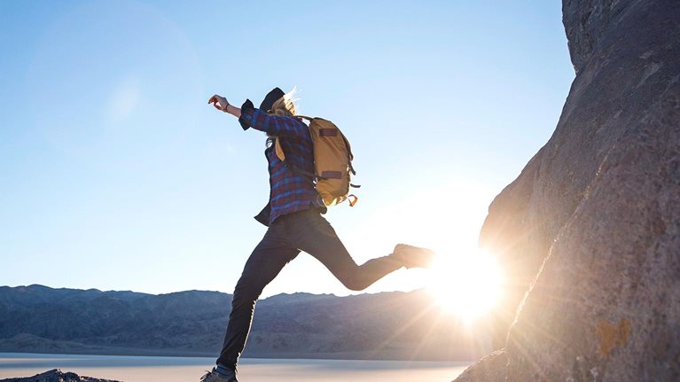 A woman jumps from one large rock to another while hiking in The Racetracks region of Death Valley.