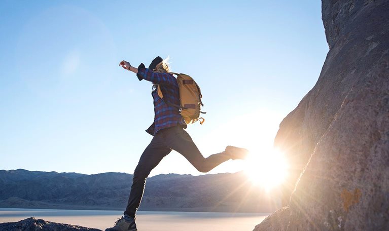 A woman jumps from one large rock to another while hiking in The Racetracks region of Death Valley.