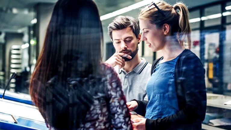 A group of printing plant engineers talking and working together at a large console