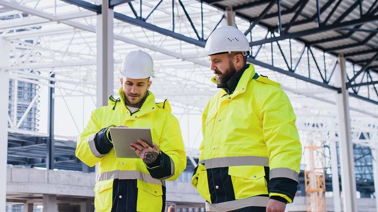 Engineers standing outdoors on construction site, using tablet.