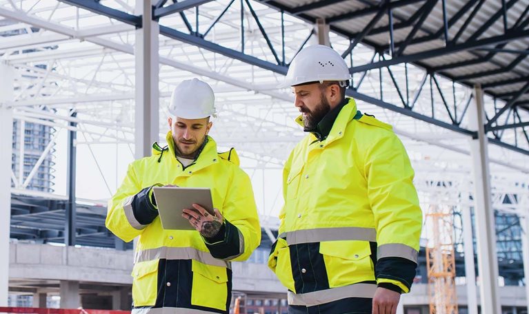 Engineers standing outdoors on construction site, using tablet.