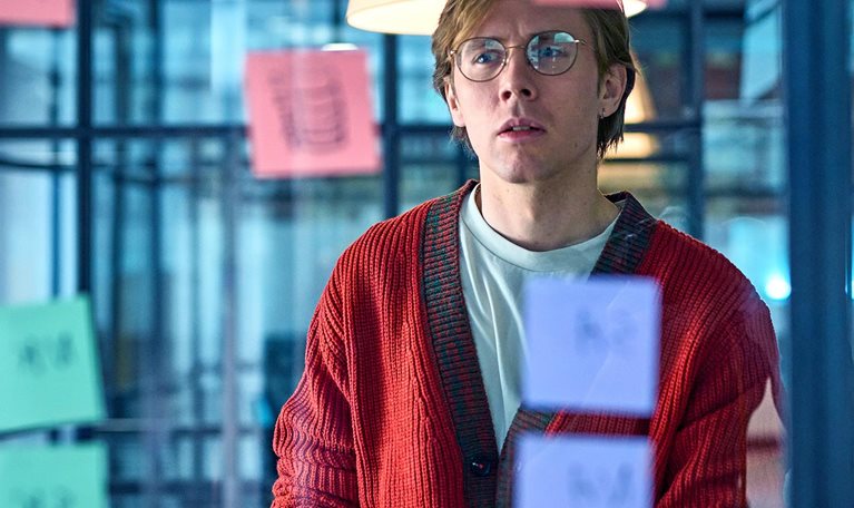 Man in his 30s wearing glasses reading post-it notes, curious expression, problem solving, planning, strategy