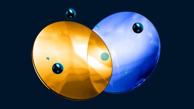 Two glass like, overlapping circular shapes—one gold and one blue—float against a dark background. Small reflective droplets are scattered across and around the surfaces.