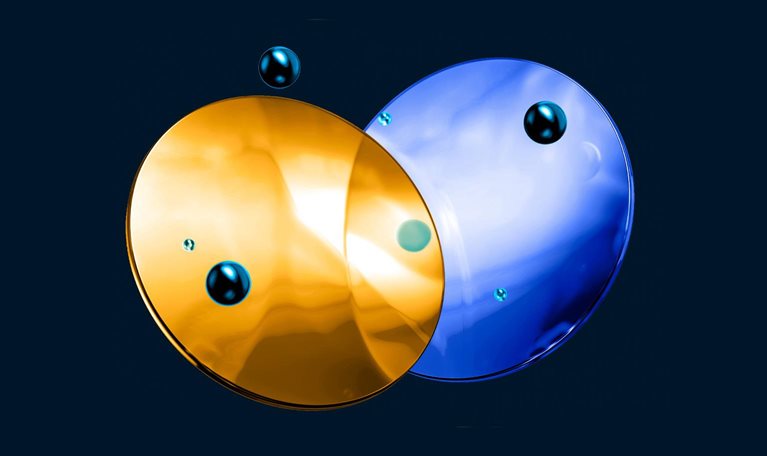 Two glass like, overlapping circular shapes—one gold and one blue—float against a dark background. Small reflective droplets are scattered across and around the surfaces.