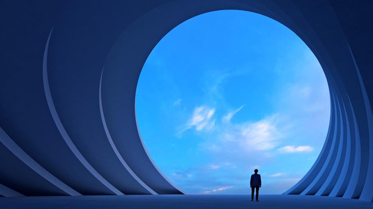 A person stands in a vast blue architectural space, looking through a large circular opening toward a bright sky.
