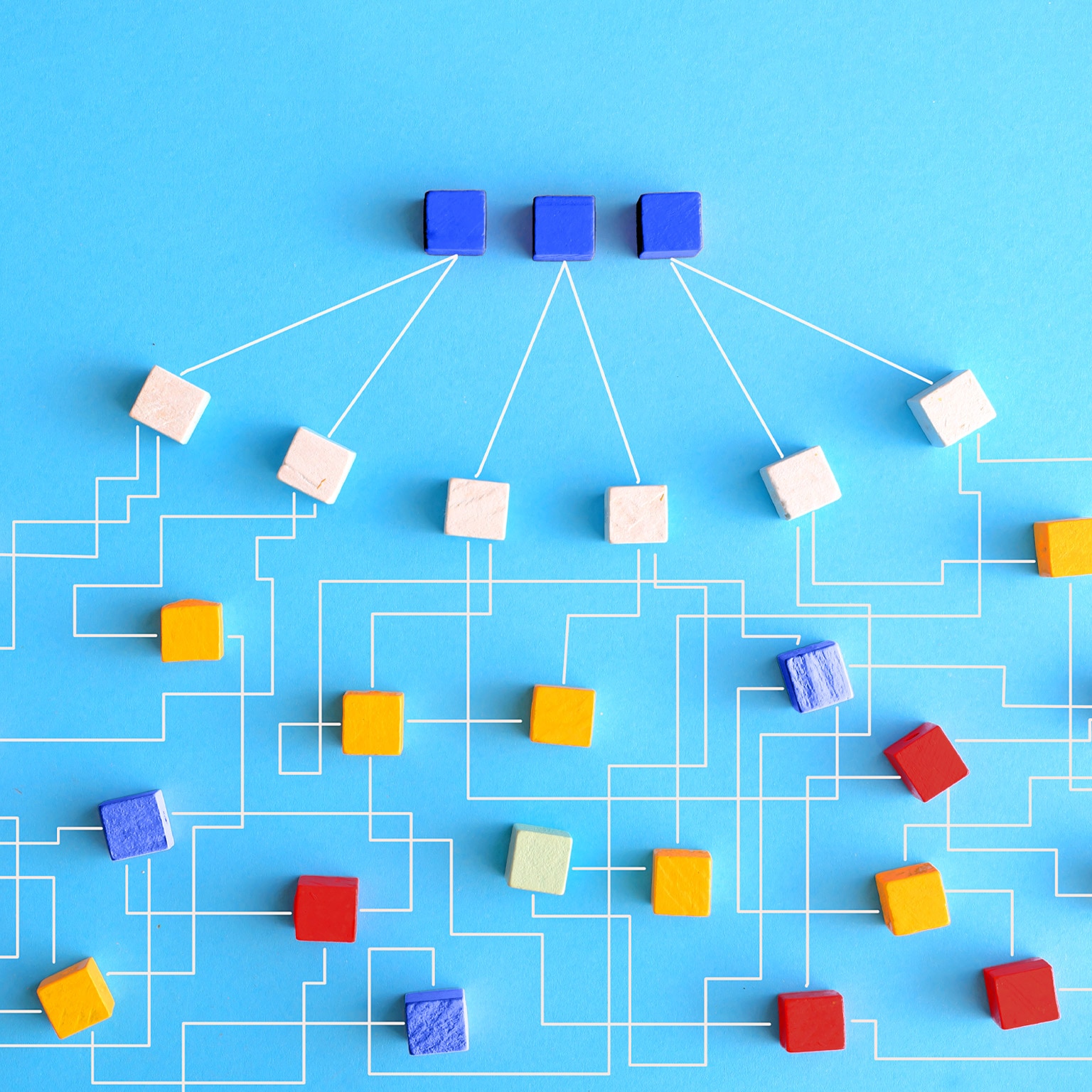 An organization chart constructed from wooden blocks that are linked together with delicate white lines. At the uppermost level of the chart, there are three blue blocks that connect to six white blocks. These white blocks then link outwards to form a larger network of blocks in varying shades of orange, red, and blue.