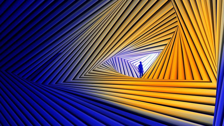 A small silhouetted figure stands inside a glowing triangular opening formed by repeating blue and orange geometric lines, creating the impression of looking through a futuristic tunnel or portal.