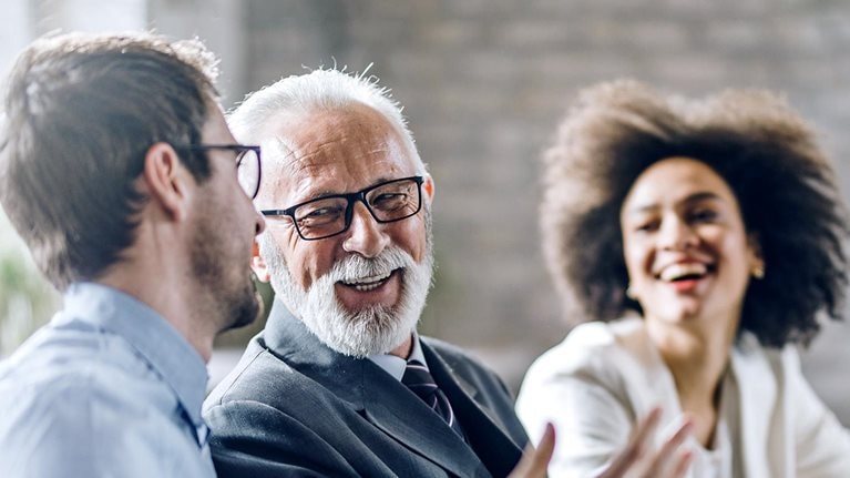 Smiling diverse business colleagues of different ages talking while working at a PC in the office.