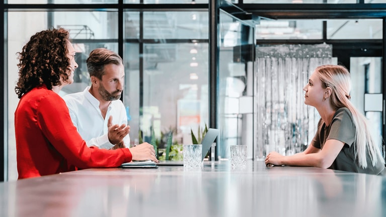 Three people converse at a desk