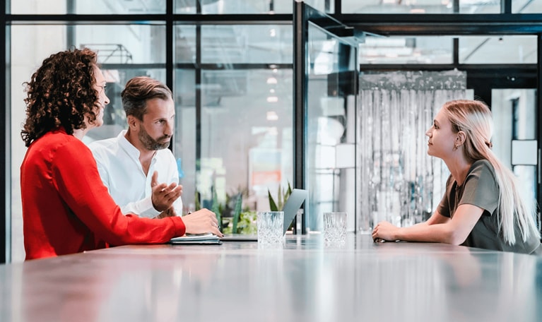 Three people converse at a desk
