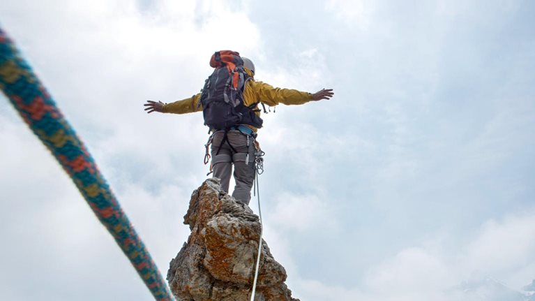 Mountaineer standing on a peak, wearing a harness