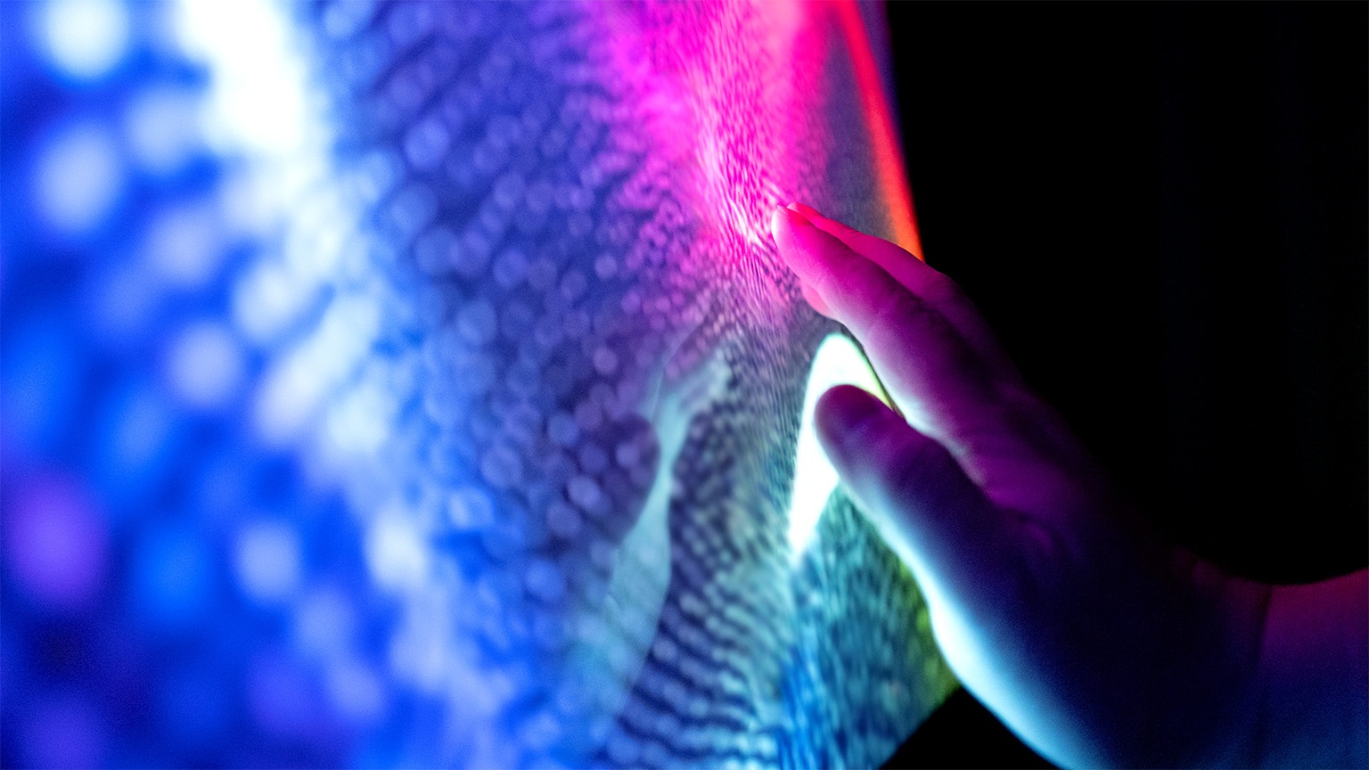 Image of a hand touching glowing pixels on a screen.