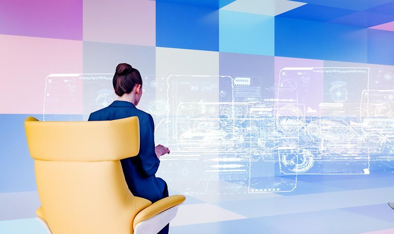 Two businesswomen sit in modern chairs facing a large, translucent screen displaying complex data visualizations. The futuristic setting suggests a collaborative work environment utilizing advanced technology.