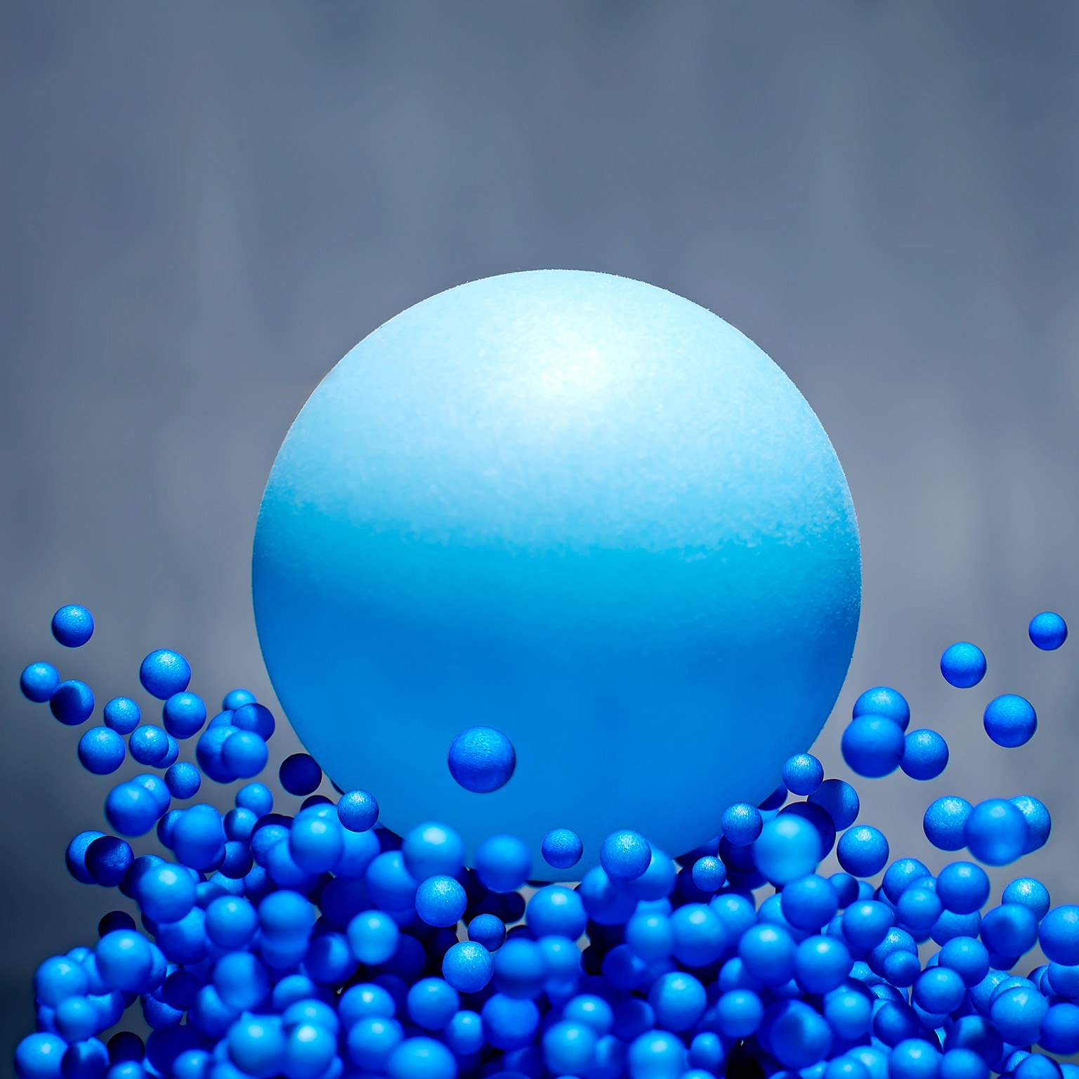 A 3D illustration of a large blue ball splashing into many, much smaller, blue balls