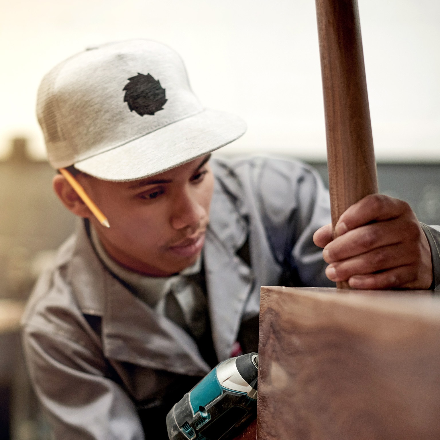 A young male carpenter attaching a wooden leg to a wood table