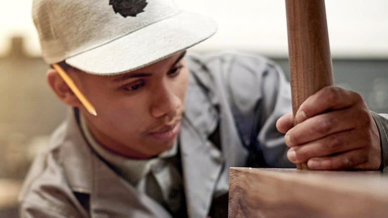 A young male carpenter attaching a wooden leg to a wood table