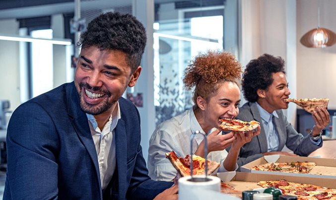 A photo of three people laughing and eating pizza
