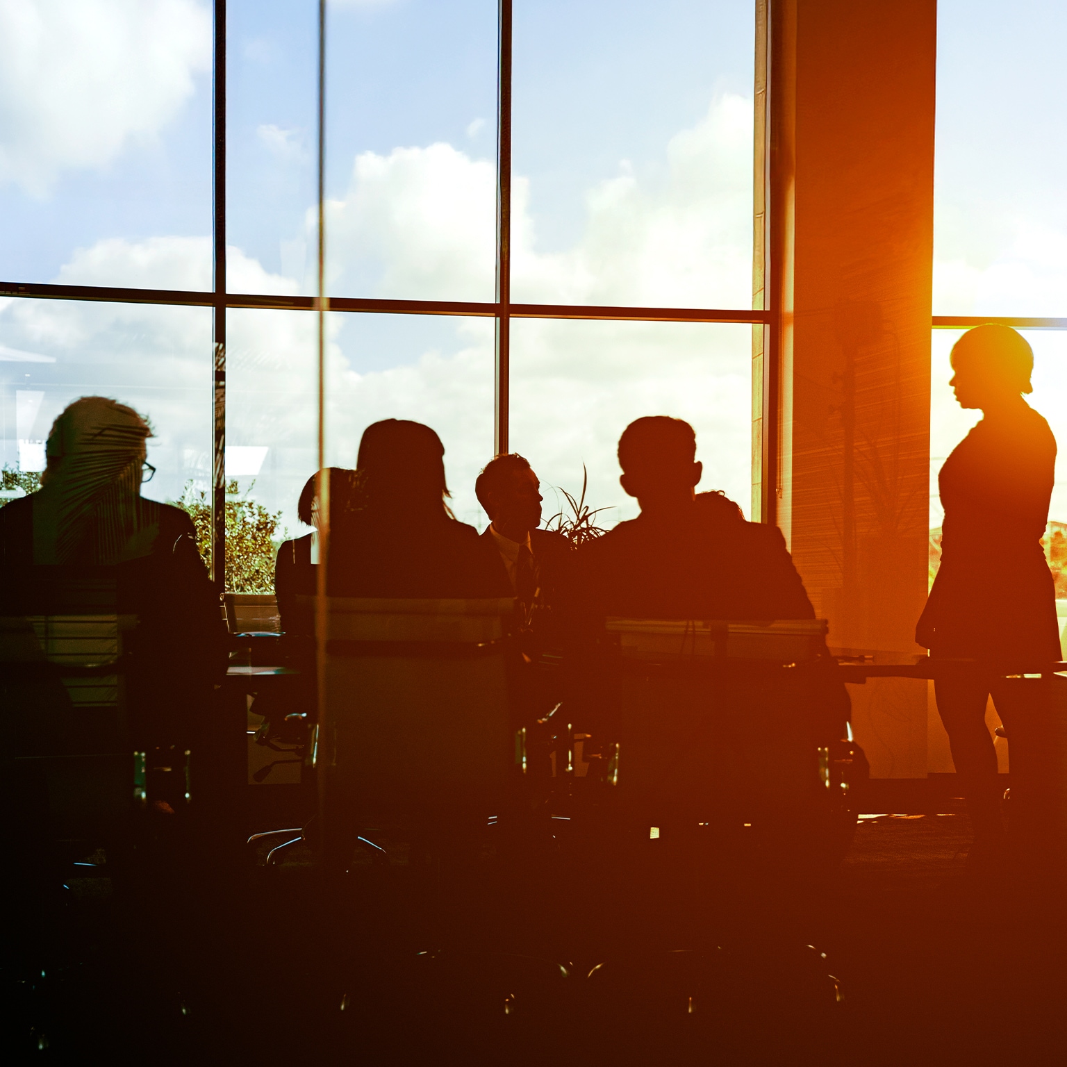 The sun is setting on workers in glass-walled boardroom