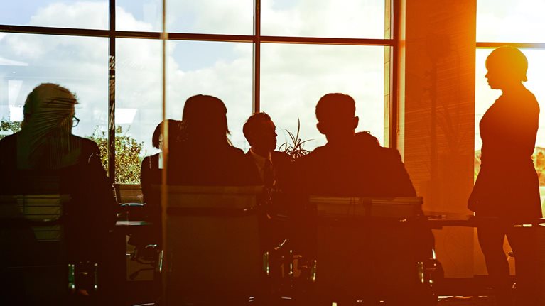 The sun is setting on workers in glass-walled boardroom