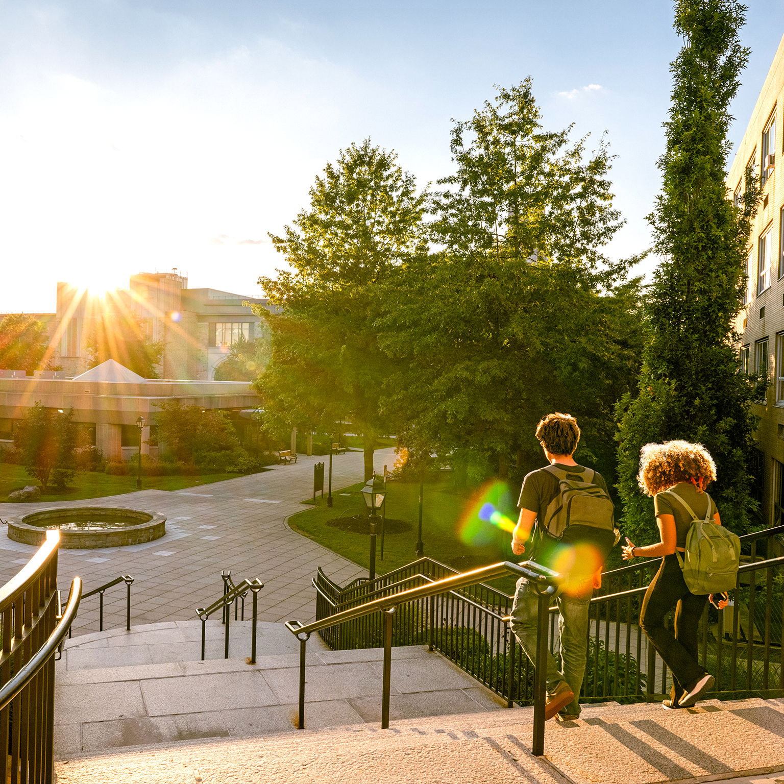 Rear view of two university students walk down campus stairs at sunset