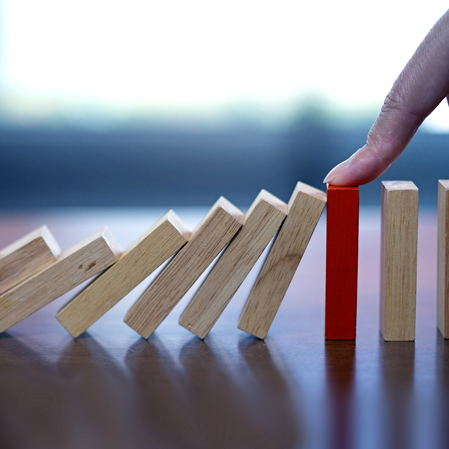 Close up image of a finger reaching down and stopping falling dominos.